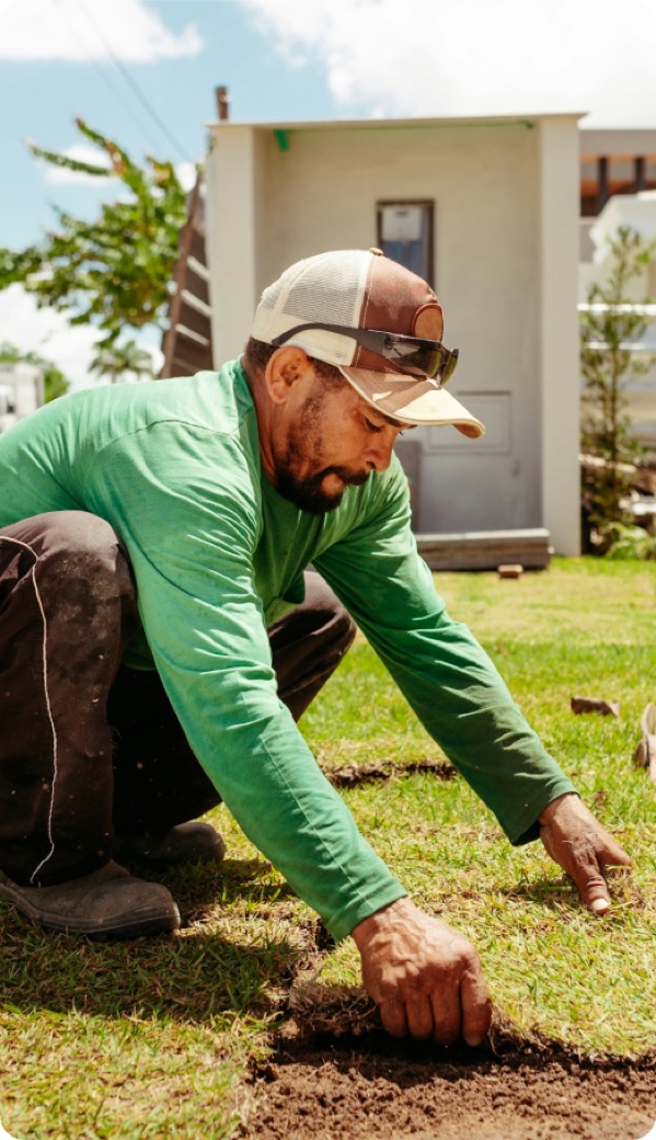 A landscaper laying fresh sod on a suburban front lawn, both hands in the soil.